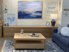 Coastal wooden coffee table in a living room setting, featuring decorative items and a blue sofa, with wall art depicting a coastal scene, emphasizing Coastal Design Furniture's custom furniture offerings.