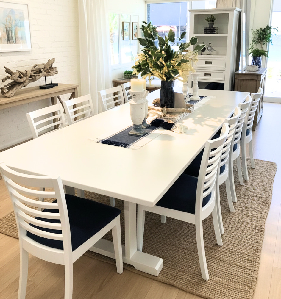 Modern coastal dining table set with black table and white upholstered dining chairs in an open-plan living area